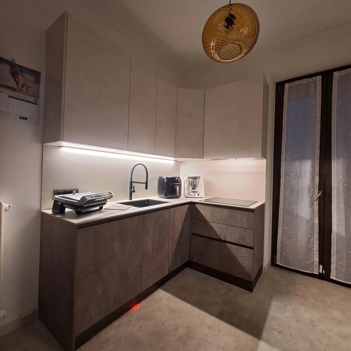 Cucina ad angolo con ante effetto pietra e illuminazione sottopensile in un'abitazione del pinerolese